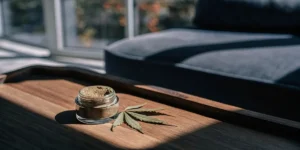 Glass jar of kief with cannabis leaf on wooden tray in bright living room.
