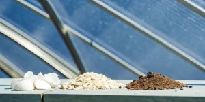 Three piles of gardening materials: white eggshells, light gravel, and dark soil, under a skylight.
